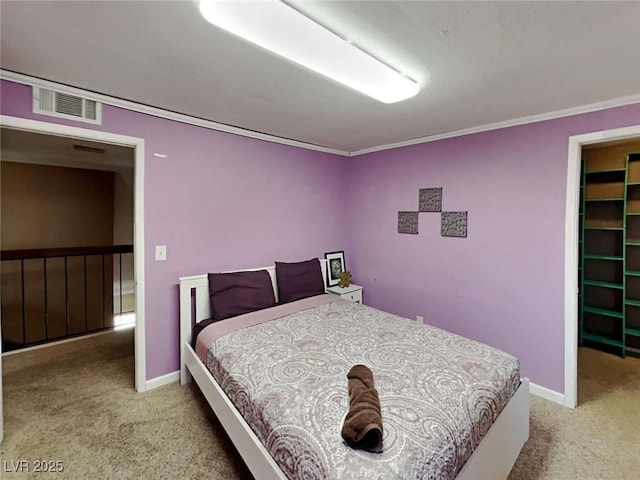 carpeted bedroom with ornamental molding, a walk in closet, visible vents, and baseboards