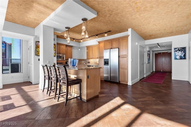 kitchen with stainless steel appliances, decorative backsplash, stone countertops, a kitchen breakfast bar, and baseboards