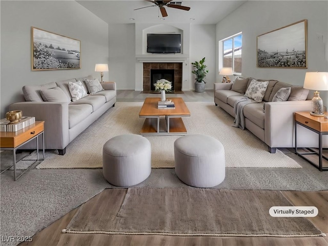 living room featuring a tile fireplace, ceiling fan, and wood finished floors