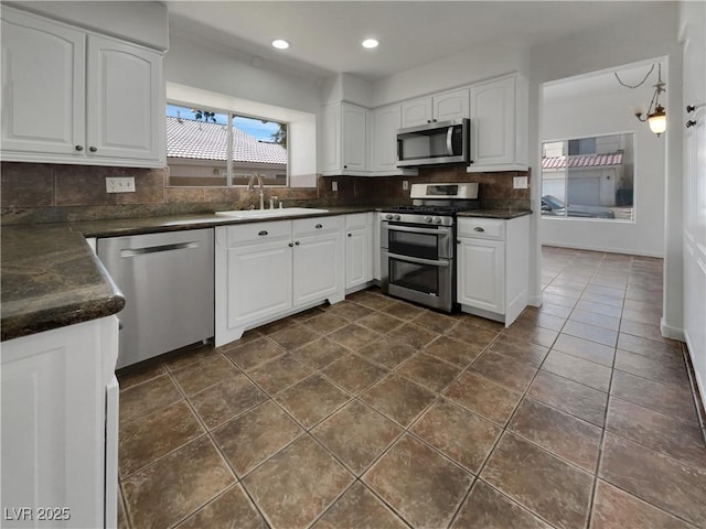 kitchen with appliances with stainless steel finishes, dark countertops, a sink, and tasteful backsplash