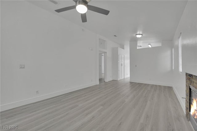 unfurnished living room featuring light wood finished floors, visible vents, a glass covered fireplace, ceiling fan, and baseboards