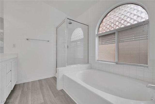 bathroom with a stall shower, wood finished floors, vanity, and a bath