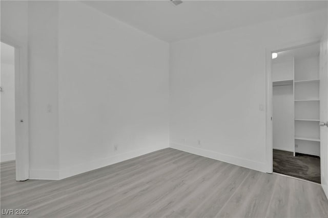 unfurnished bedroom featuring a walk in closet, a closet, baseboards, and wood finished floors