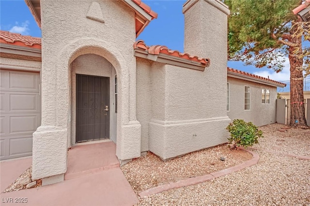 view of exterior entry with a tile roof, a chimney, and stucco siding