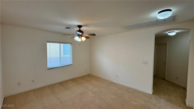 spare room with light carpet, baseboards, visible vents, and arched walkways