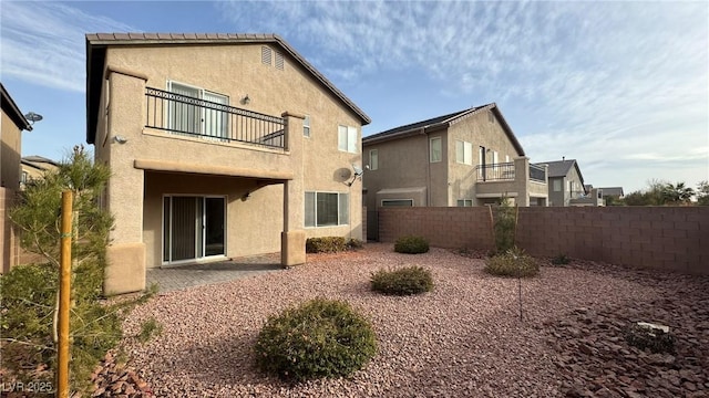 rear view of house featuring a patio area, fence private yard, a balcony, and stucco siding