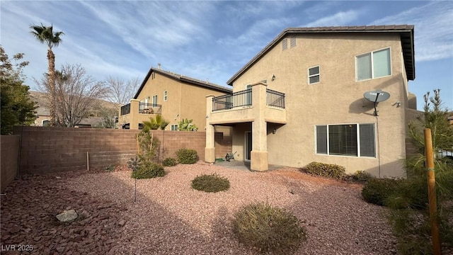 rear view of house with a fenced backyard, a balcony, and stucco siding