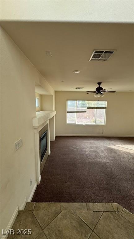 unfurnished living room featuring visible vents, dark carpet, a tiled fireplace, a ceiling fan, and baseboards