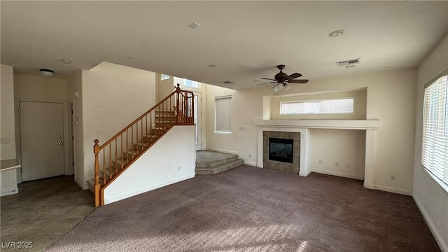 unfurnished living room featuring visible vents, stairway, a tiled fireplace, ceiling fan, and baseboards