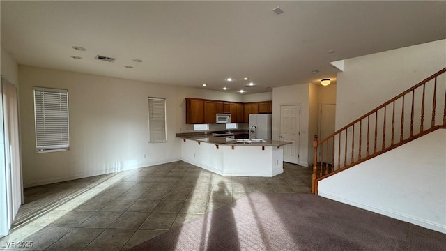 kitchen with white refrigerator with ice dispenser, dark countertops, recessed lighting, a peninsula, and a kitchen bar