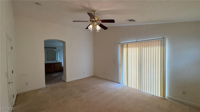 carpeted spare room featuring arched walkways, ceiling fan, visible vents, baseboards, and vaulted ceiling