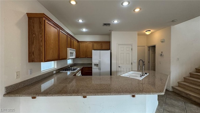 kitchen featuring white appliances, stone countertops, visible vents, a peninsula, and a sink