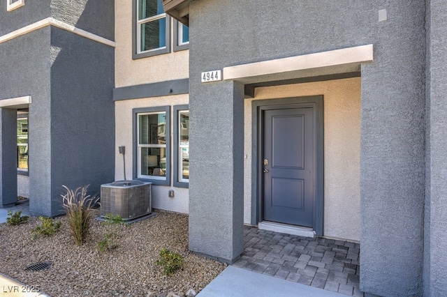 doorway to property with central AC unit and stucco siding