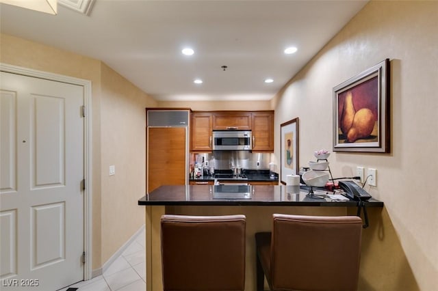 kitchen with dark countertops, stainless steel microwave, brown cabinets, a peninsula, and recessed lighting