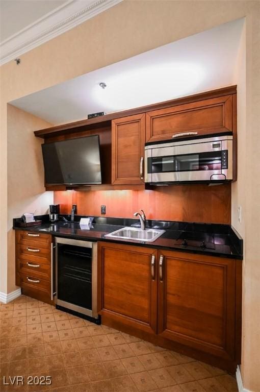 kitchen featuring beverage cooler, dark countertops, stainless steel microwave, brown cabinets, and a sink