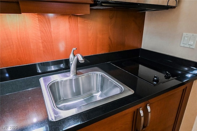 kitchen featuring black electric stovetop, brown cabinetry, dark countertops, and a sink