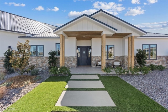 view of exterior entry featuring metal roof, stone siding, board and batten siding, and stucco siding