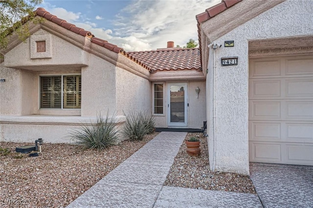 entrance to property featuring an attached garage, stucco siding, and a tiled roof