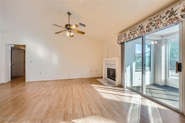 unfurnished living room featuring ceiling fan, a tile fireplace, visible vents, vaulted ceiling, and light wood finished floors