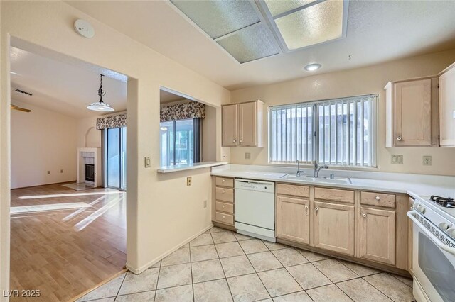 kitchen featuring a fireplace, light tile patterned floors, a sink, white appliances, and plenty of natural light