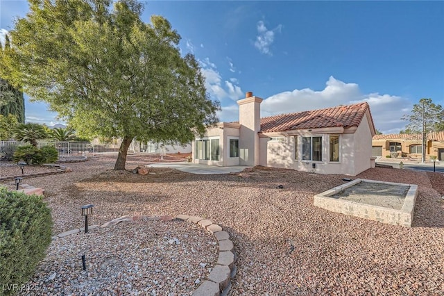 rear view of property featuring a chimney, fence, a tiled roof, and stucco siding