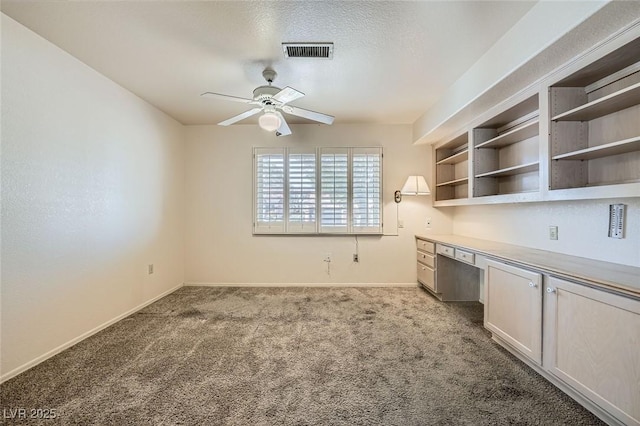 unfurnished office with light carpet, baseboards, visible vents, ceiling fan, and built in desk