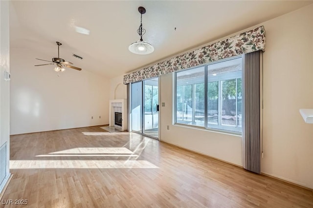 unfurnished living room featuring lofted ceiling, visible vents, a tiled fireplace, a ceiling fan, and wood finished floors