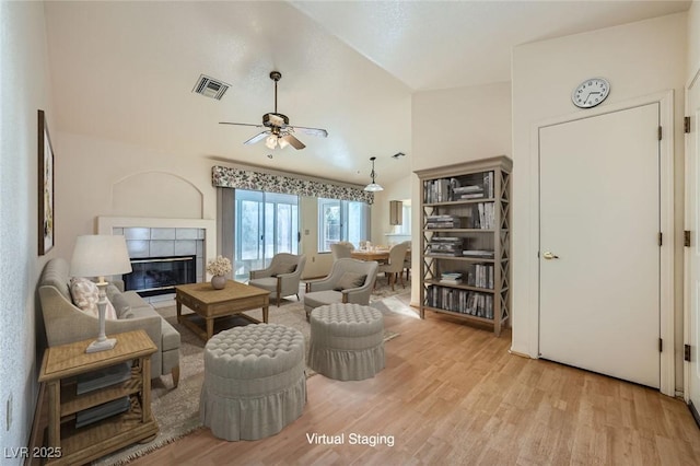 living room with ceiling fan, a tile fireplace, wood finished floors, and visible vents