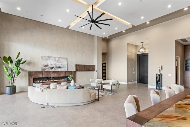 living room with baseboards, a towering ceiling, recessed lighting, and a glass covered fireplace