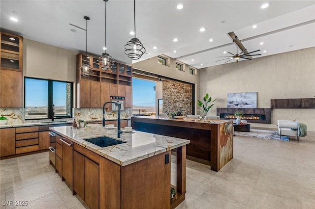 kitchen with ceiling fan, tasteful backsplash, a sink, a large island, and a glass covered fireplace