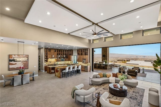 living area featuring baseboards, a notable chandelier, a high ceiling, and recessed lighting