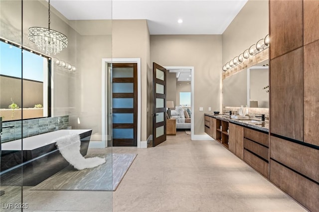 ensuite bathroom with a soaking tub, baseboards, double vanity, connected bathroom, and an inviting chandelier