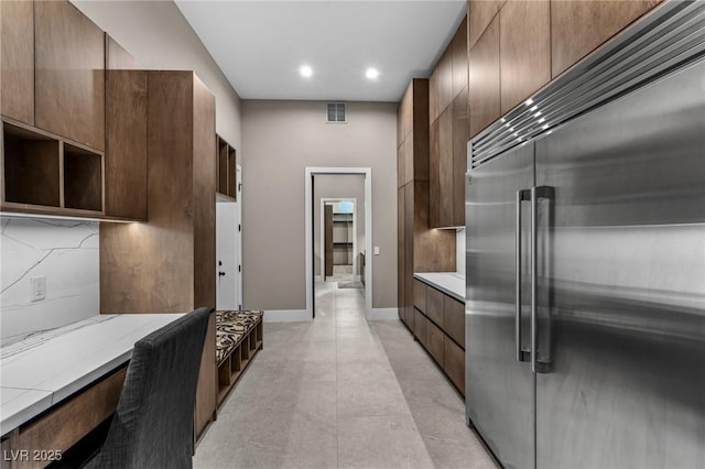 kitchen with decorative backsplash, stainless steel built in refrigerator, visible vents, and light countertops