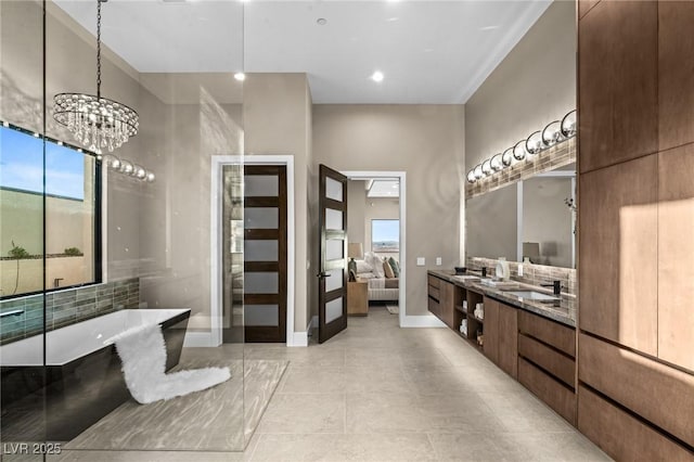 full bathroom featuring a sink, baseboards, a freestanding bath, double vanity, and an inviting chandelier