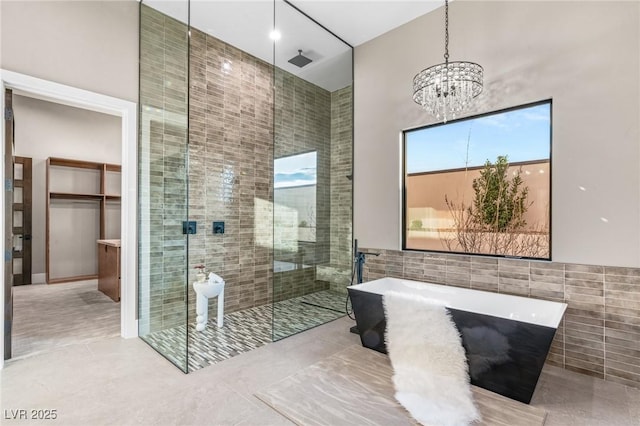 full bath featuring a shower stall, a high ceiling, a freestanding bath, tile walls, and an inviting chandelier
