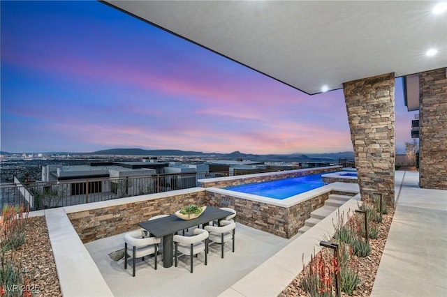pool at dusk featuring a patio, a mountain view, an in ground hot tub, and an outdoor pool