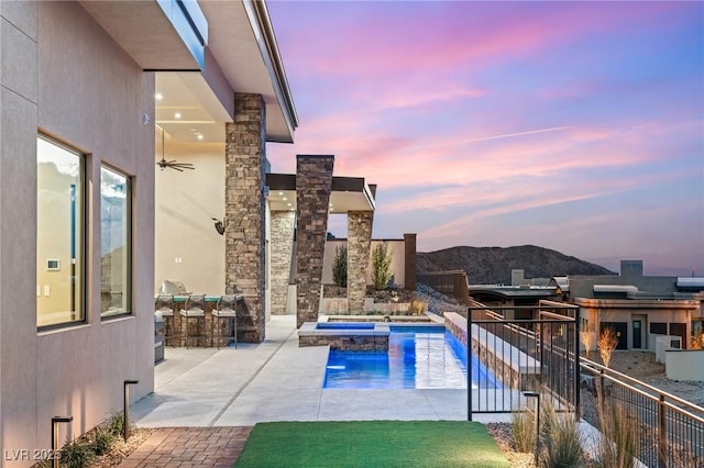 pool at dusk featuring fence, a pool with connected hot tub, a patio, and a mountain view