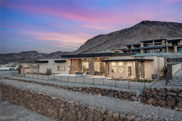 back of property at dusk with stucco siding, a mountain view, and a fenced front yard