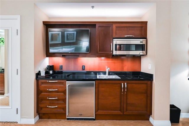 bar featuring stainless steel microwave, a sink, and baseboards