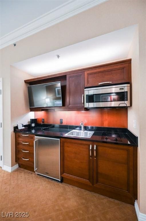 kitchen featuring baseboards, dark countertops, ornamental molding, stainless steel appliances, and a sink