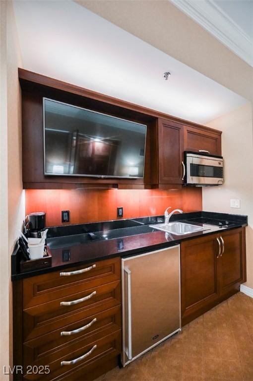 kitchen with dark countertops, stainless steel microwave, ornamental molding, a sink, and baseboards