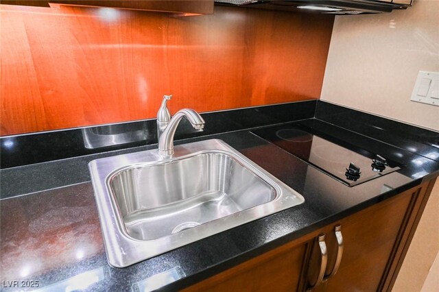 kitchen with brown cabinetry, dark countertops, a sink, and black electric stovetop