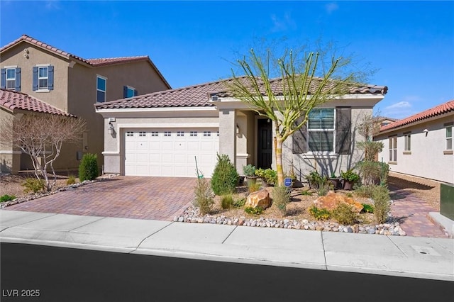 mediterranean / spanish house featuring a garage, a tile roof, decorative driveway, and stucco siding