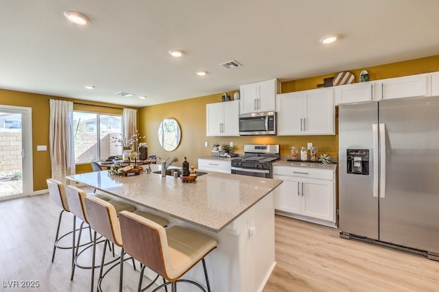 kitchen with white cabinets, light stone counters, stainless steel appliances, and a sink