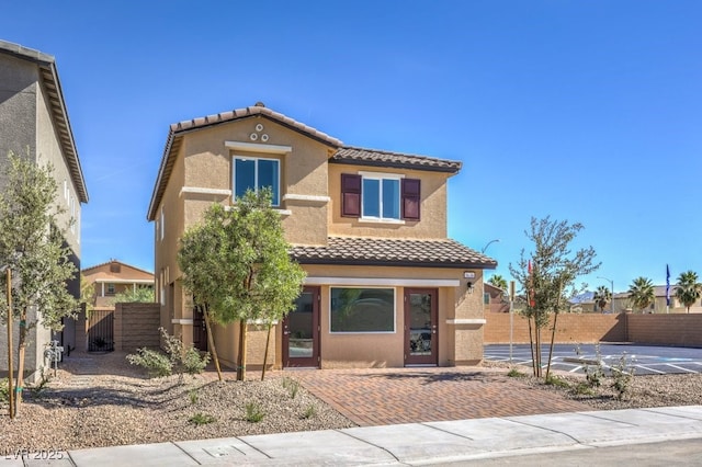 mediterranean / spanish home with a tile roof, fence, and stucco siding