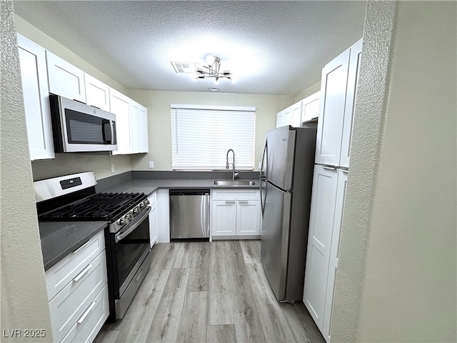 kitchen featuring visible vents, light wood-style flooring, white cabinets, stainless steel appliances, and a sink