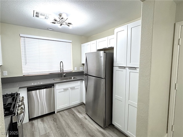 kitchen with visible vents, light wood finished floors, a sink, stainless steel appliances, and a textured ceiling