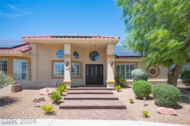 property entrance with french doors, a tile roof, solar panels, and stucco siding