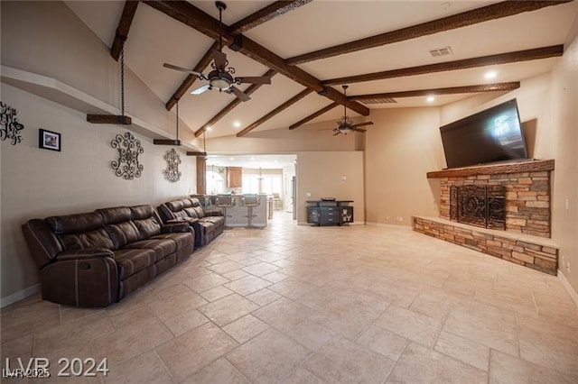 living room with a ceiling fan, beam ceiling, a stone fireplace, and baseboards