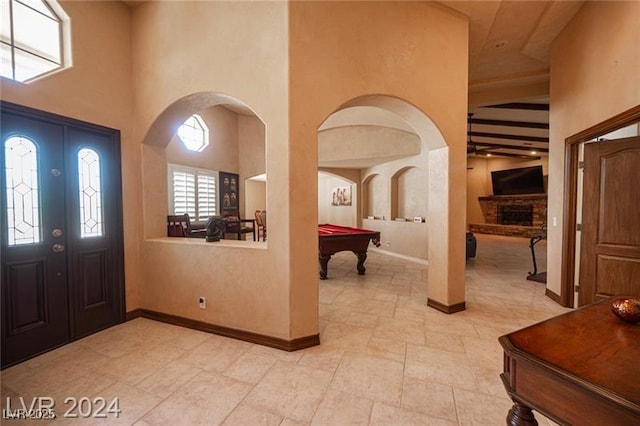 entryway with arched walkways, a fireplace with raised hearth, pool table, a towering ceiling, and baseboards